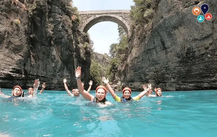 Kanyon turunda taş köprü altında berrak suda yüzen katılımcılar
